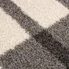 A close-up view of a shaggy rug with a geometric pattern of gray and white stripes. Náhľad obrázku produktu
