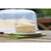 A slice of cake is on a plate with a fork and a green napkin, with a cake dome in the background. Náhľad obrázku produktu