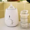 A white bottle warmer with a baby bottle on top and a stack of clear containers next to it, placed on a countertop. Produktbild-Vorschau