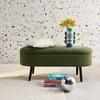 A green bouclé ottoman with a pillow and a decorative vase with flowers on top, placed in front of a terrazzo-patterned wall. Produktbild-Vorschau