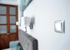 A close-up shot of a light switch on a white wall, with a headboard and sconces visible in the background. Anteprima dell’immagine prodotto