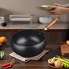 A wok pan with a wooden handle is placed on a kitchen counter, surrounded by fresh ingredients like carrots, chili peppers, mushrooms, and green peppers. Produktbild-Vorschau