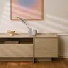 A modern TV cabinet with a minimalist design, featuring wooden drawers and an open shelf, decorated with a vase and a decorative bowl. A framed abstract painting hangs on the wall above. Produktbild-Vorschau