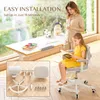 A mother and daughter are in a bright room with a large window. The daughter is sitting in a desk chair and reading a book. The desk has art supplies on it. A smaller inset image shows the parts of the desk chair. Produktbild-Vorschau