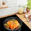 A close-up view of a Tefal frying pan with salmon and vegetables cooking on an induction hob, with kitchen storage jars in the background. Produktbild-Vorschau