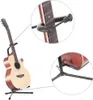 An acoustic guitar is displayed on a black stand, with close-up insets showing the capo and the stand's base. Náhľad obrázku produktu