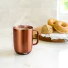 A steaming bronze mug sits on a kitchen counter next to donuts and bread. Voir les images du produit