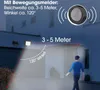 A solar-powered floodlight with a motion sensor is shown illuminating an outdoor area at night, with a person walking into the illuminated zone. Produktbild-Vorschau