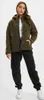 A woman wearing a green fleece jacket and black pants stands against a white background. Produktbild-Vorschau