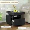 A black nightstand with drawers and open shelves, placed next to a sofa in a living room setting. The image highlights various storage features with text labels. Podgląd zdjęcia produktu