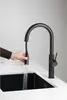 A hand is holding a black kitchen faucet, and water is running from it into a black sink. Náhľad obrázku produktu