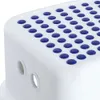 Close-up view of a white step stool with blue non-slip dots on its surface. Two oval holes are visible on the side of the stool. Náhled obrázku produktu