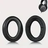 Two black headphone ear pads are shown against a white background. A pair of black headphones is visible in the upper right corner. Produktbild-Vorschau