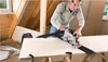 A man is using a circular saw to cut a piece of wood in an attic. Podgląd zdjęcia produktu