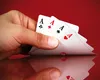 A hand holding four aces of playing cards against a red background. Produktbild-Vorschau