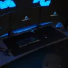 A gaming setup with multiple monitors, a keyboard, mouse, and mousepad, illuminated by blue LED lighting. Produktbild-Vorschau