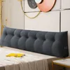 A long, tufted, wedge-shaped headboard cushion is placed on a bed against a wall with decorative art. Produktbild-Vorschau