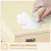 A hand is wiping a spill off a light-colored wooden surface with a cloth. The image is part of a marketing graphic for a pet product. Náhled obrázku produktu