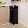 A black trash can with a motion sensor lid is placed next to a tan cabinet in a kitchen. Podgląd zdjęcia produktu