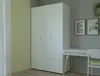 A white wardrobe with drawers next to a desk and chair in a room. Produktbild-Vorschau