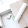 A roll of white shelf liner on a light wood surface, with a drawer partially open showing some cosmetic items. Produktbild-Vorschau