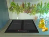 A modern kitchen induction cooktop with a backsplash featuring hanging herbs, next to a pitcher of lemonade and lemons. Produktbild-Vorschau