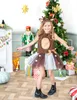 A young girl dressed as a deer poses in front of a Christmas tree and fireplace. Anteprima dell’immagine prodotto