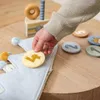 A child's hand is placing a numbered disc onto a fabric crown, with a toy birthday cake in the background. Podgląd zdjęcia produktu