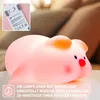 A pink pig-shaped night light is shown on a surface, with a blurred background of pillows and lights. Podgląd zdjęcia produktu