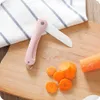 A pink ceramic folding knife is shown on a wooden cutting board next to sliced carrots and a white striped cloth. Voir les images du produit