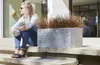 A woman sits on steps next to a planter with ornamental grass. Náhľad obrázku produktu