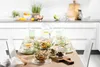 A table set for a meal with various glass bowls, plates, and a pitcher of water. Anteprima dell’immagine prodotto