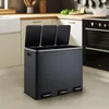 A dark gray triple-compartment trash can is shown in a modern kitchen setting. Voir les images du produit