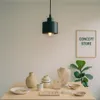 A display of jewelry and decorative items on a wooden table, with a pendant light fixture overhead and a framed sign in the background. Produktbild-Vorschau