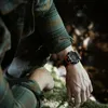 A person wearing a watch in an outdoor, natural setting. Produktbild-Vorschau