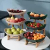 A multi-tiered fruit stand with various fruits and pastries displayed on a white table. Náhled obrázku produktu