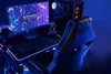 A gaming setup with a chair, desk, computer, and monitor, illuminated by blue and purple lights. Produktbild-Vorschau
