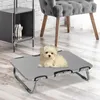 A small white dog sits on a gray elevated pet bed in a room with wooden flooring and a brick wall. Voir les images du produit