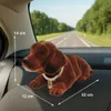 A brown dachshund toy dog is lying on the dashboard of a car, with a road and trees visible in the background. Produktbild-Vorschau