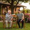 Two men are sitting on a wooden bench in a garden, toasting with beer. Produktbild-Vorschau