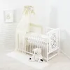 A baby crib set up in a room with white brick walls and a light wooden floor. Voir les images du produit