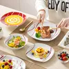 A table setting with various porcelain dishes filled with food, and a person's hands using cutlery to eat from one of the plates. Produktbild-Vorschau
