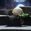A collectible rubber duck toy resembling the character Nemesis from Resident Evil, holding a green weapon, sitting on concrete steps. Podgląd zdjęcia produktu