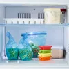 A freezer shelf with various food storage items, including bags of frozen peas and carrots, an ice cube tray, and containers. Produktbild-Vorschau