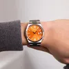 A person wearing a grey sweater is showing a Citizen watch with an orange dial on their wrist. Voir les images du produit