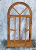 A rusted metal decorative window frame with an arched top and opening shutters, placed against a textured wall. Produktbild-Vorschau