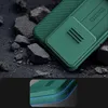 A close-up view of a green phone case with a textured back and a sliding camera cover, resting on dark, rocky ground. Produktbild-Vorschau