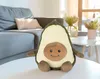 A plush avocado toy is placed on a white table in a living room setting, with a sofa and decorative plants in the background. Anteprima dell’immagine prodotto