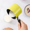 A hand is pouring milk from a yellow saucepan into a clear glass bowl. Náhled obrázku produktu
