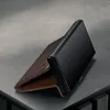 A dark brown leather phone case is shown open, with a black smartphone inside, propped up on a textured gray surface. Anteprima dell’immagine prodotto